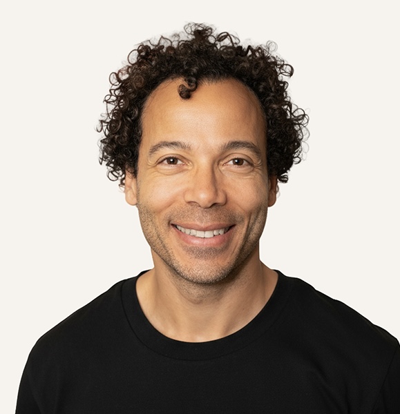 Portrait of Serge Alleyne, smiling, in a black t-shirt